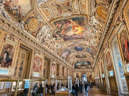 The Apollo Gallery interior at the Louvre Museum in Paris showing ornate 17th-century ceiling paintings and gilded decoration, now reopened without jewels on display after the 2024 heist
